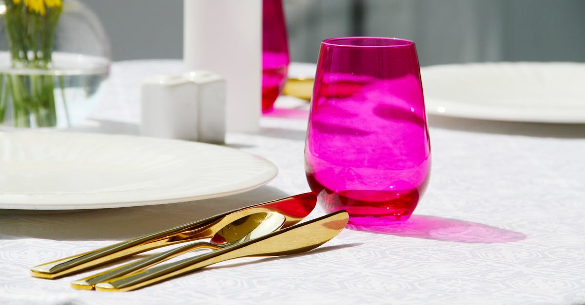 Chic dining table setup featuring golden cutlery, a pink glass, and vibrant yellow flowers for an elegant touch.