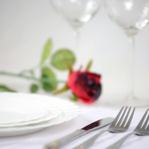 An elegant table setup featuring a red rose, cutlery, and wine glasses for a romantic dinner.