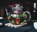 A glass teapot with herbal tea, surrounded by cups and a cookie, creating a cozy atmosphere.