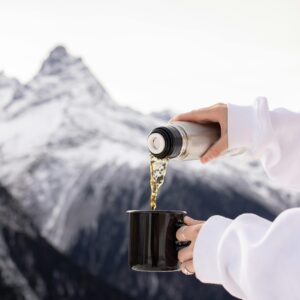 A hot beverage being poured into a mug against a snowy mountain backdrop.